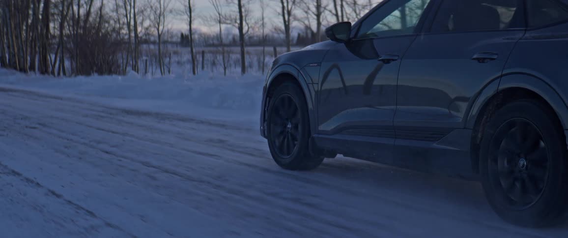 A vehicle driving on a snowy road with the sky and clouds in the background