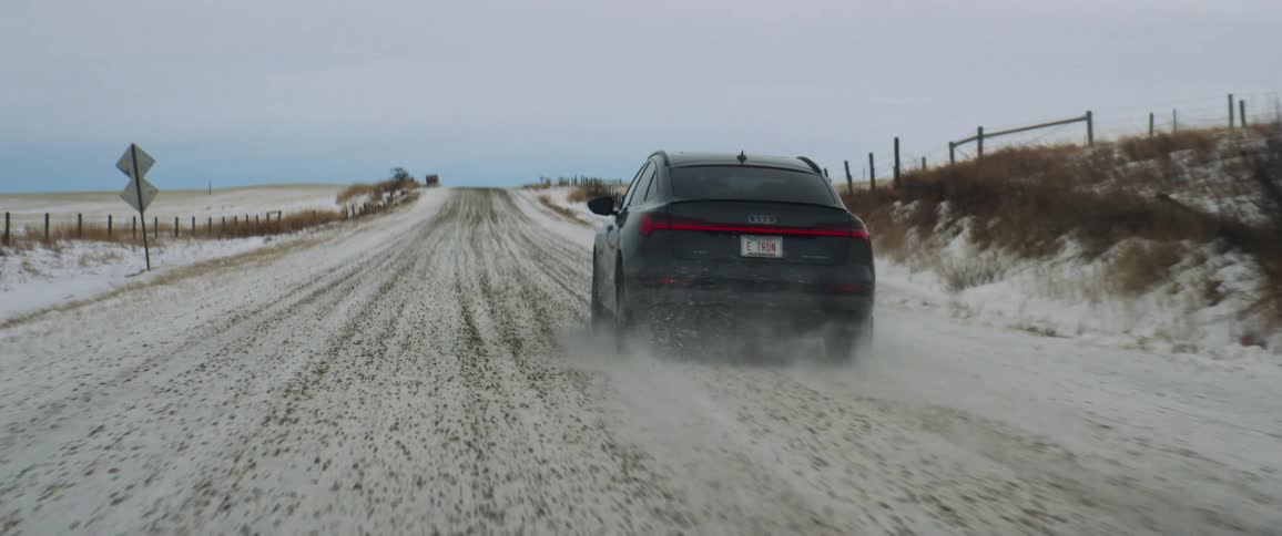Dark grey audi car drives snowy uphill in the countryside