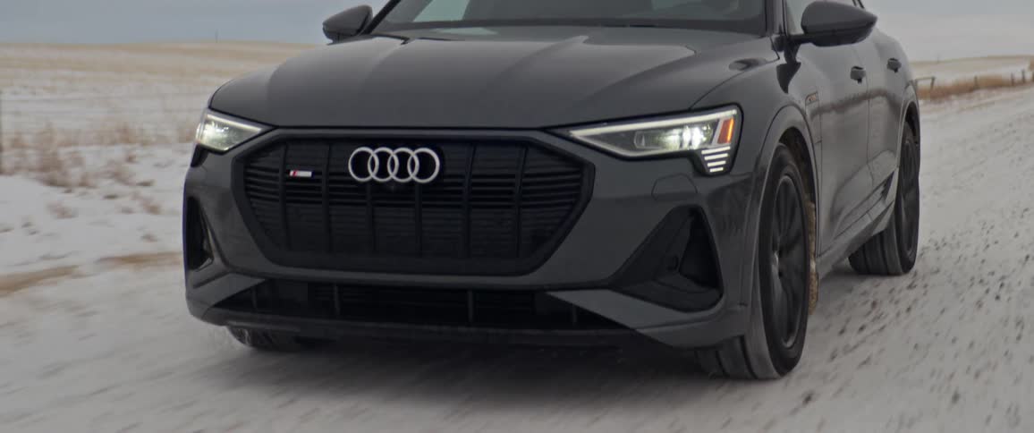 A black audi automobile travels on a snow covered road