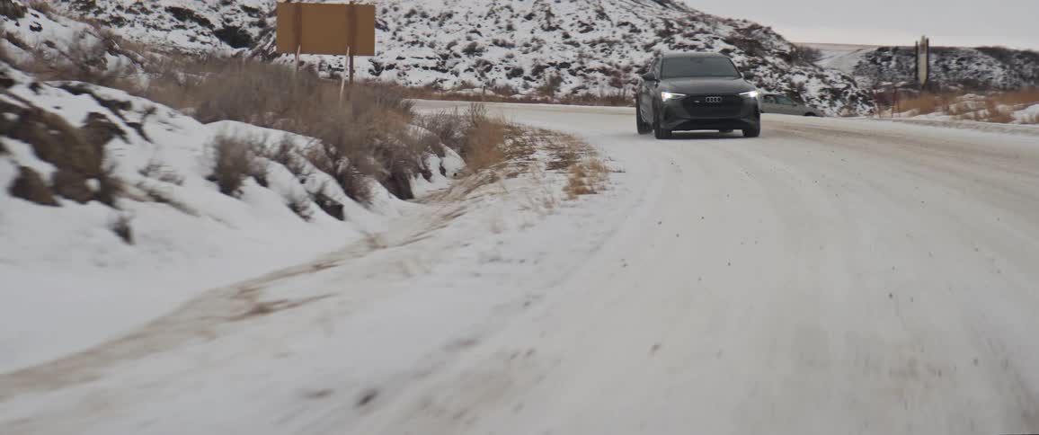 A vehicle drives on a snow dusted hillside road