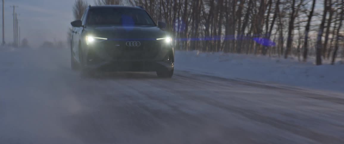 A vehicle driving on a snowy road with trees the sky and clouds in the background