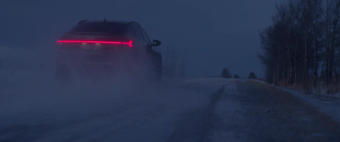 A vehicle driving on a snowy road with trees the sky and clouds in the background