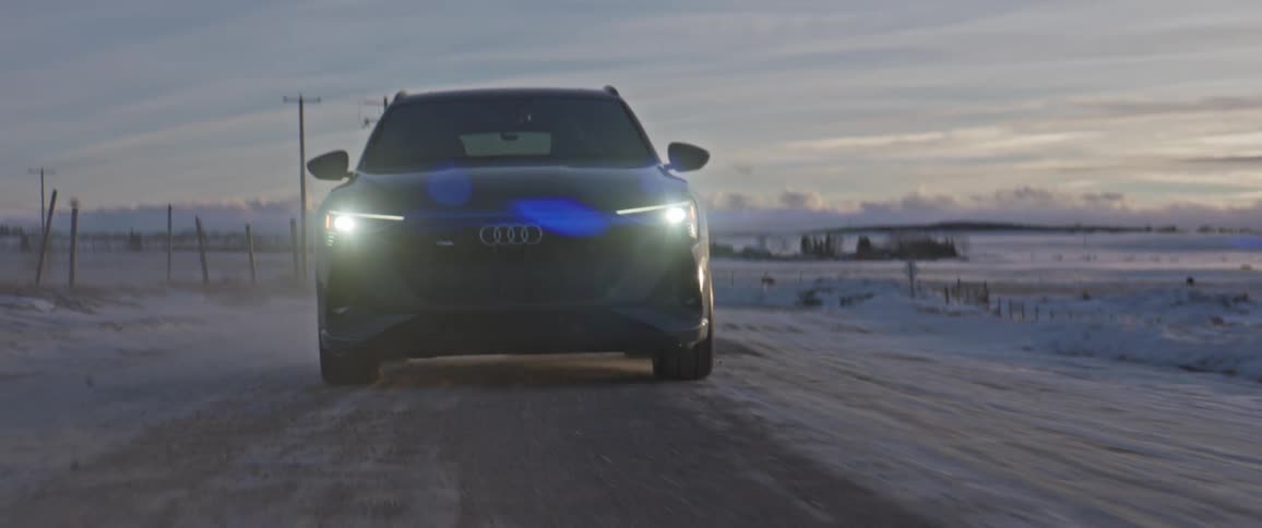 Audi car drives on snowy road in the field at dusk