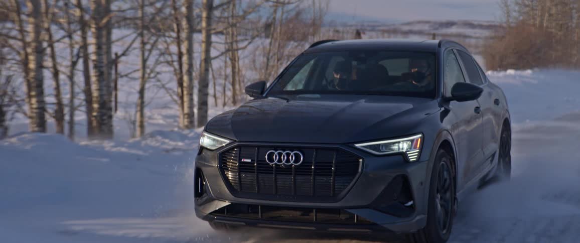 A black audi car travels on a snow covered road with trees along the roadside