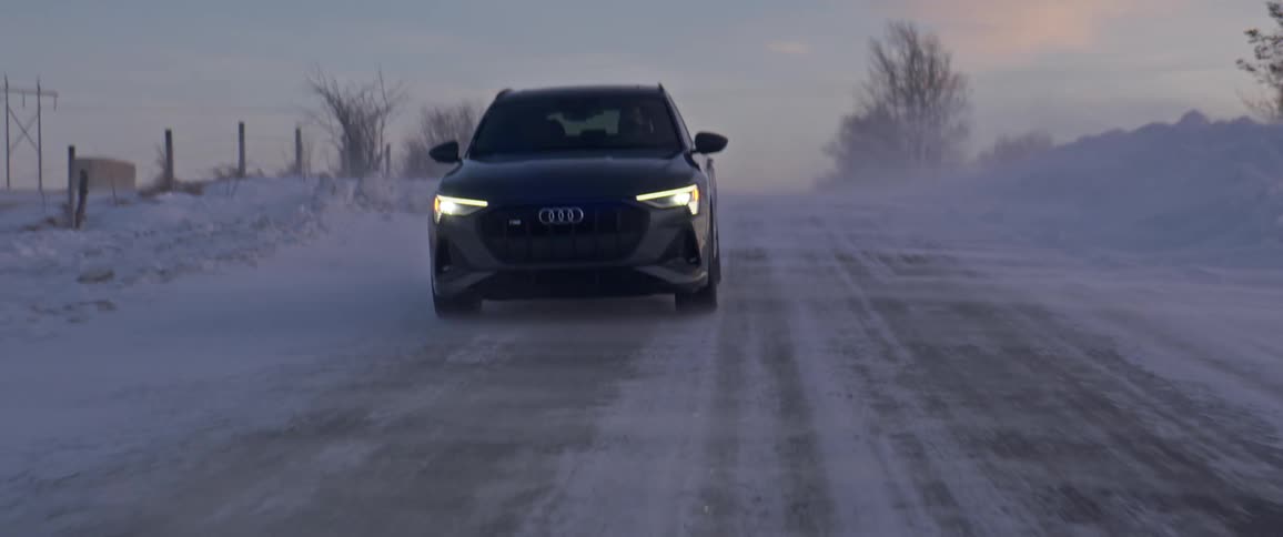 Black car with headlights on driving on a snow covered road in the countryside at morning