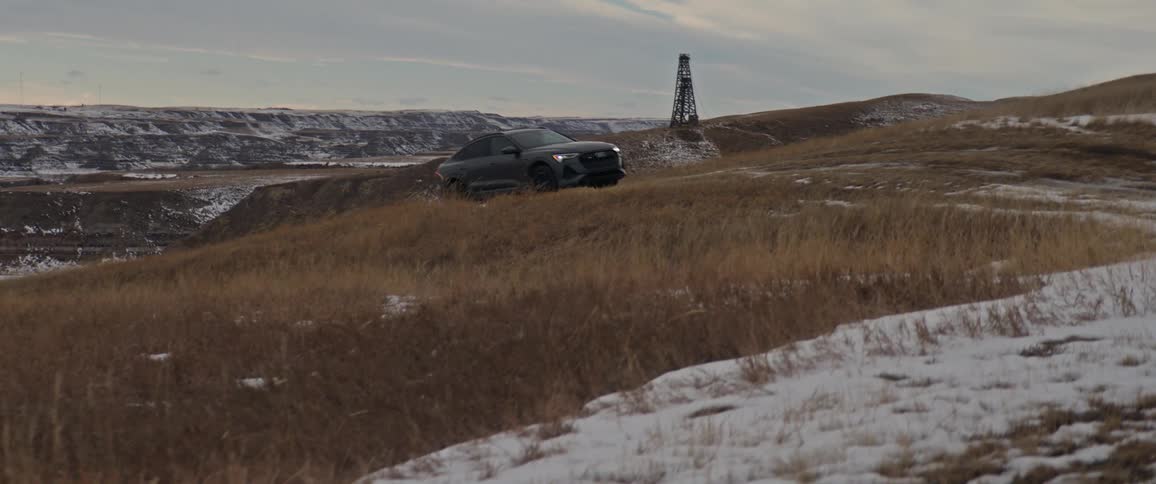 A vehicle driving on a snowy landscape with grass with the sky and clouds in the background