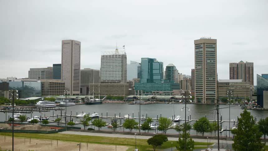 The city of Baltimore with buildings and trees with a marina with boats with the sky and clouds in the background