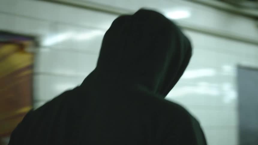 A man walks through a subway terminal with his hoodie up