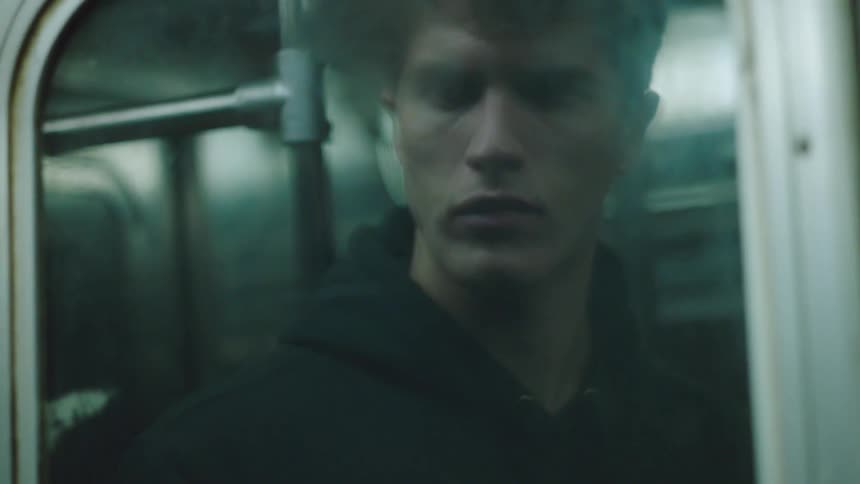 A mans views his own reflection in the door window of a moving subway train
