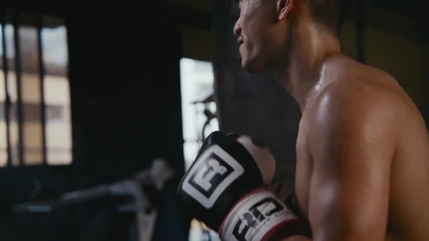 An asian man practicing boxing with another man inside a gym