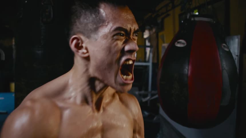 Strong shirtless muscular man screams while standing inside a gym