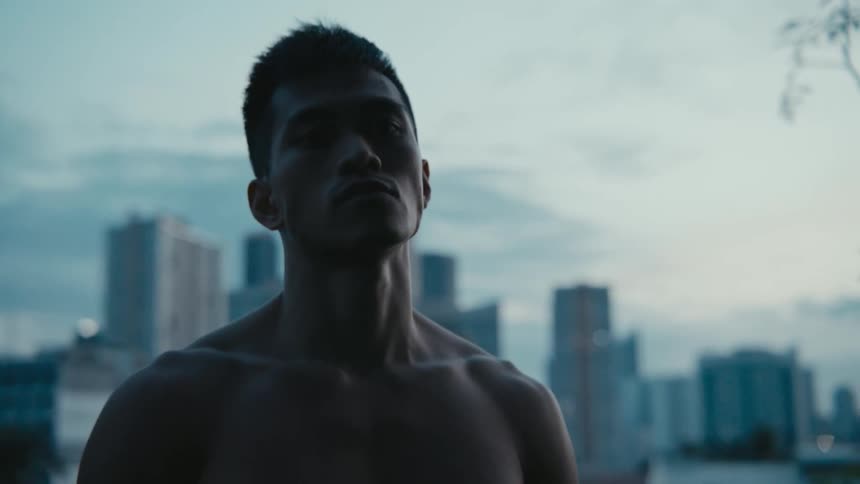 A shirtless man stands in front of a cityscape