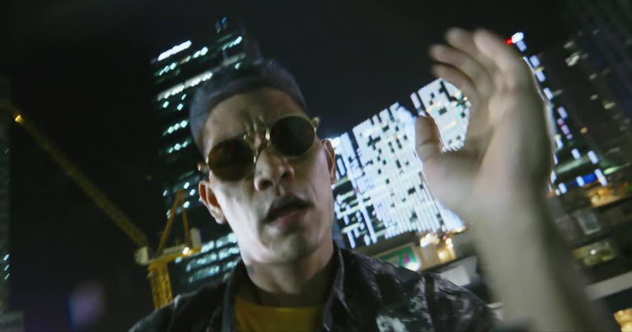 Dancer wearing sunglasses dancing in front of buildings in the city at night, looking at the camera