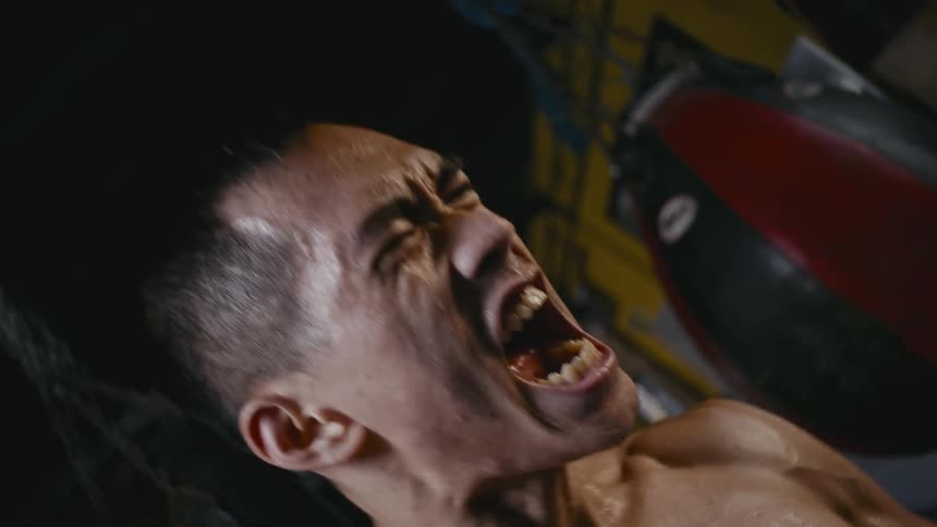 An asian man with well built muscles roars with aggression