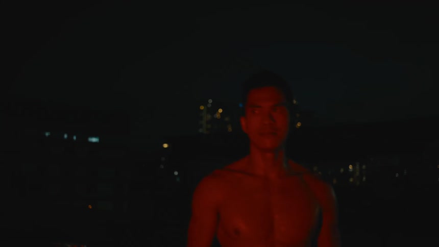 Strong muscular shirtless asian man screaming violently near the city at night