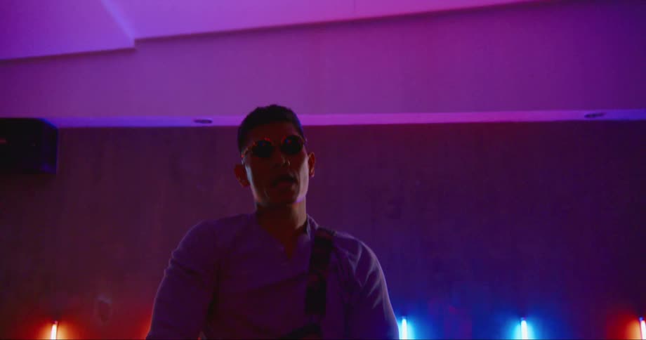 A man with sunglasses in a room dancing with a wall and lights in the background