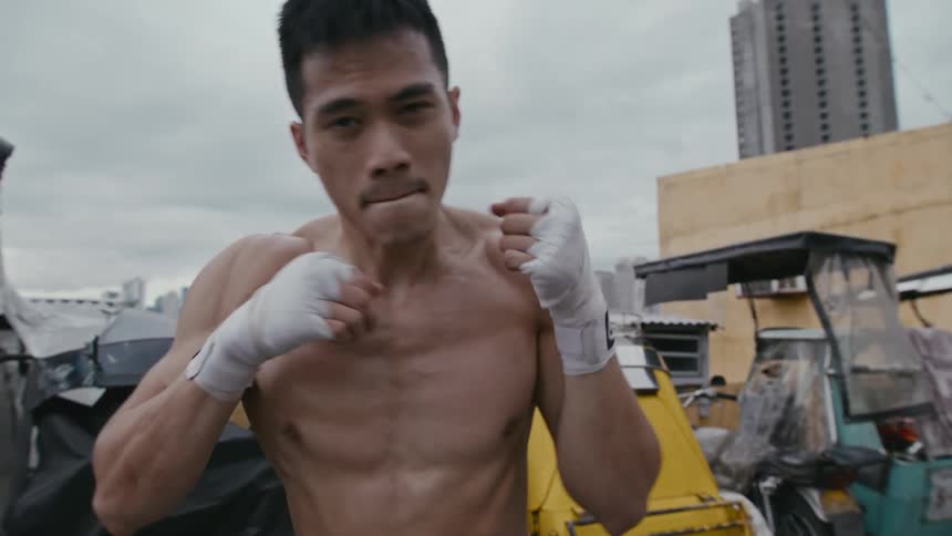 Man throws punches as he shadowboxes in parking lot next to vehicles with city skyline in background