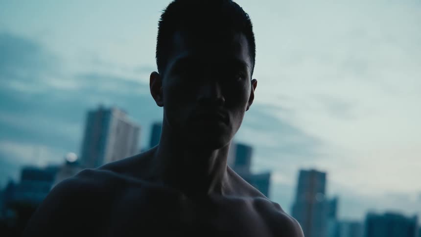 Young shirtless muscular man staring at the camera in front of the city skyline