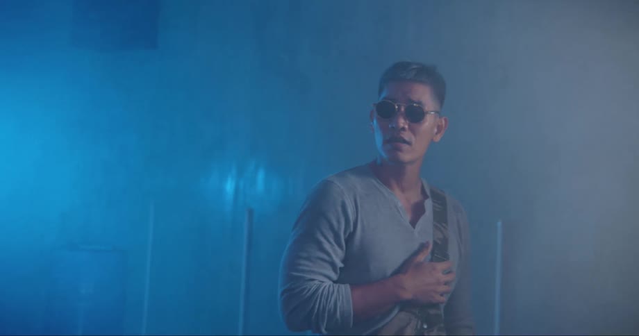 A man with sunglasses in a room singing with a wall in the background