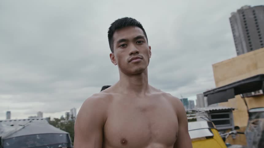Young shirtless muscular man staring at the camera in front of the city skyline
