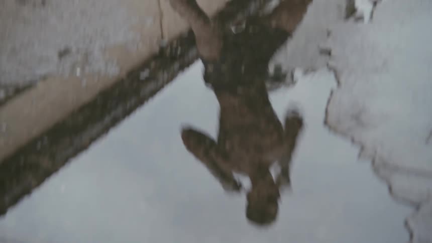 A male boxer practices outside and his reflection is seen in a puddle on the ground