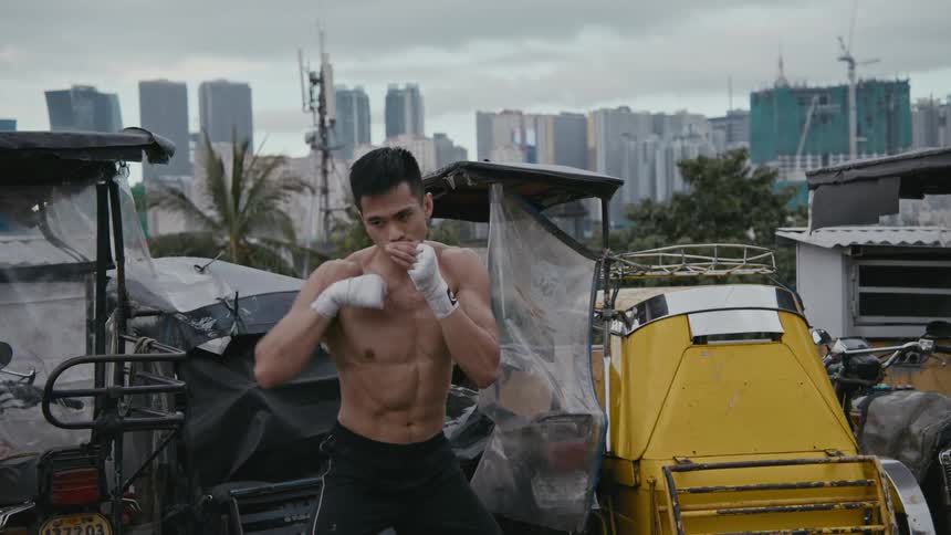A man boxes on a roof top with the city skyline in the distance