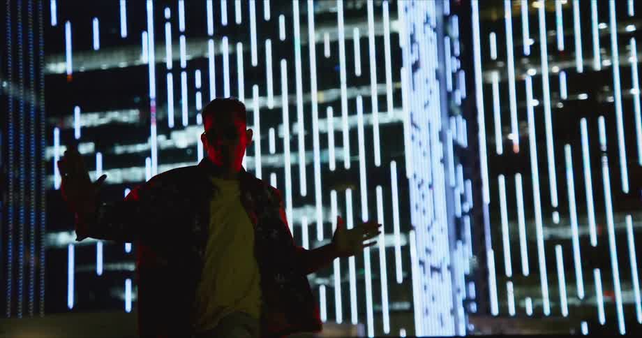 A teenage boy jumps and spins around in front of a lit up building in a city