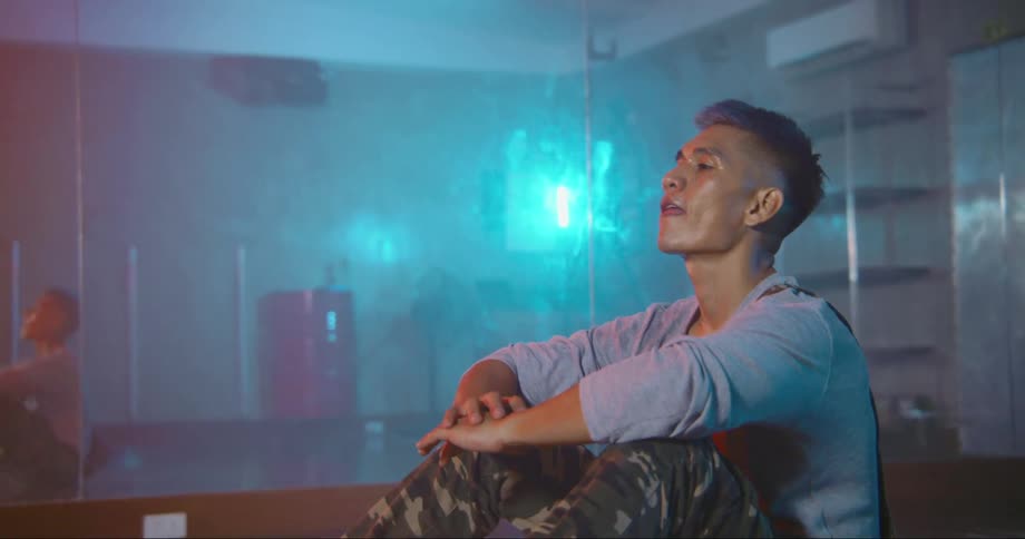 A man in a room sitting on the floor with a wall and a mirror in the background