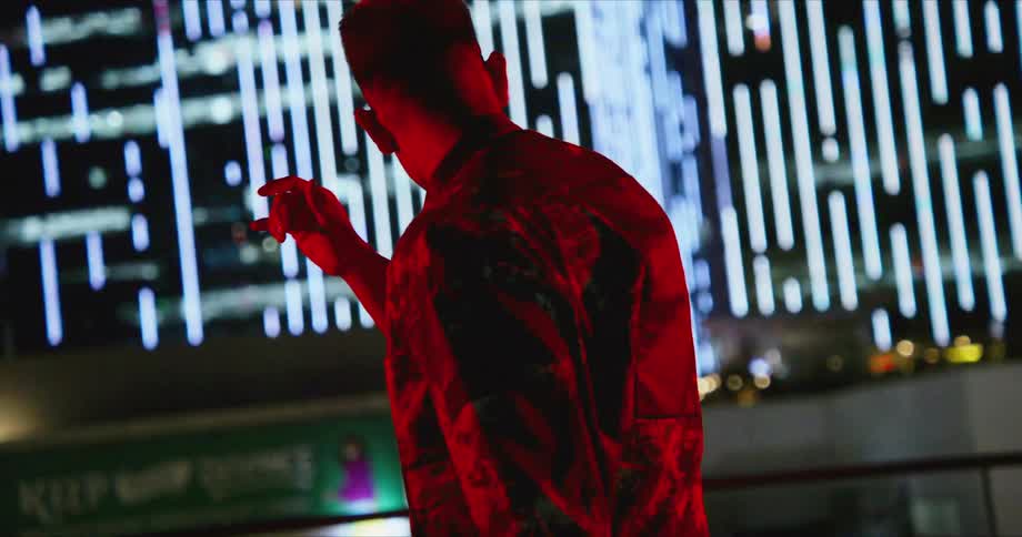 A man reaches up to touch his glasses as he stands near a downtown building