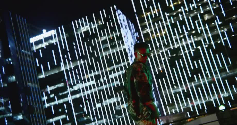 A man with sunglasses dancing on a rooftop with buildings in the background