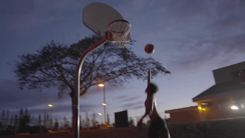 Two men are playing basketball at sunset