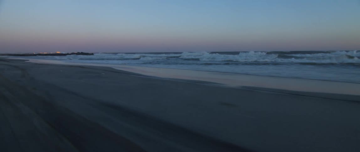 A beach with sand and waves with the ocean sky and clouds in the background