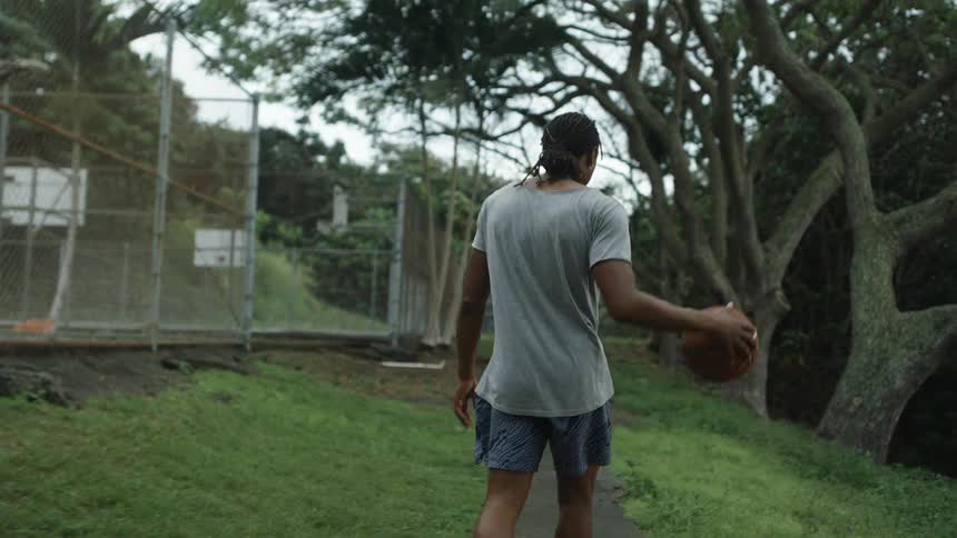 A man dribbles a basketball as he walks down a sidewalk outside basketball courts