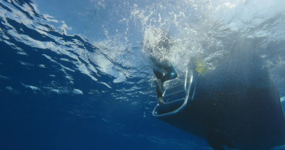 Scuba diver uses a stair to board a boat in the ocean
