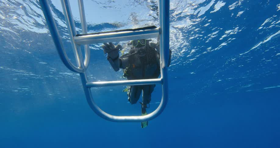 A person with scuba gear swimming underwater with bubbles next to a boat