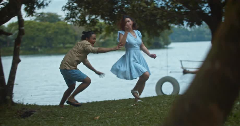 Man and woman play chase on riverbank on slightly misty day