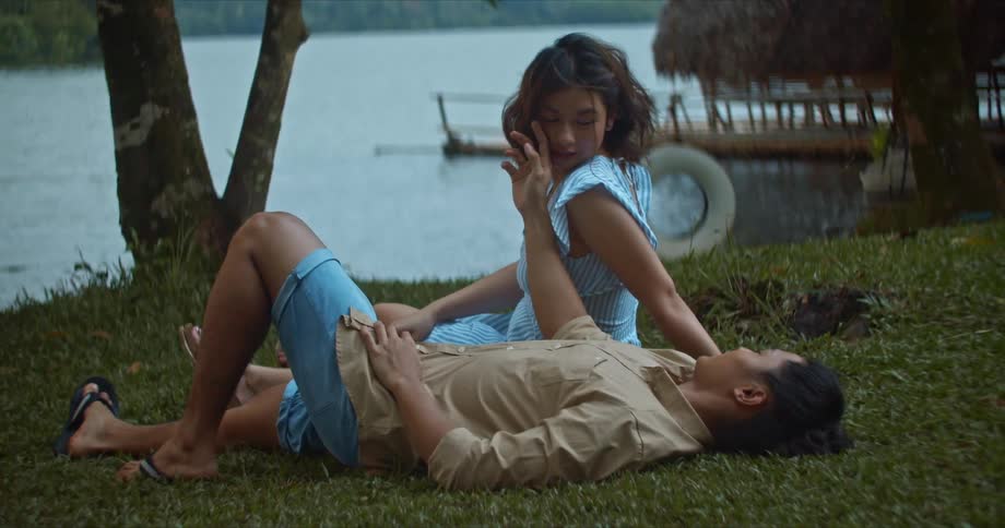 Couple resting on the grass near a lake at daytime