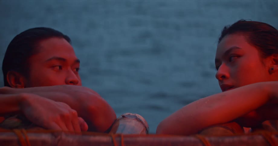 A man and a woman hanging on to a raft with a body of water rippling in the background