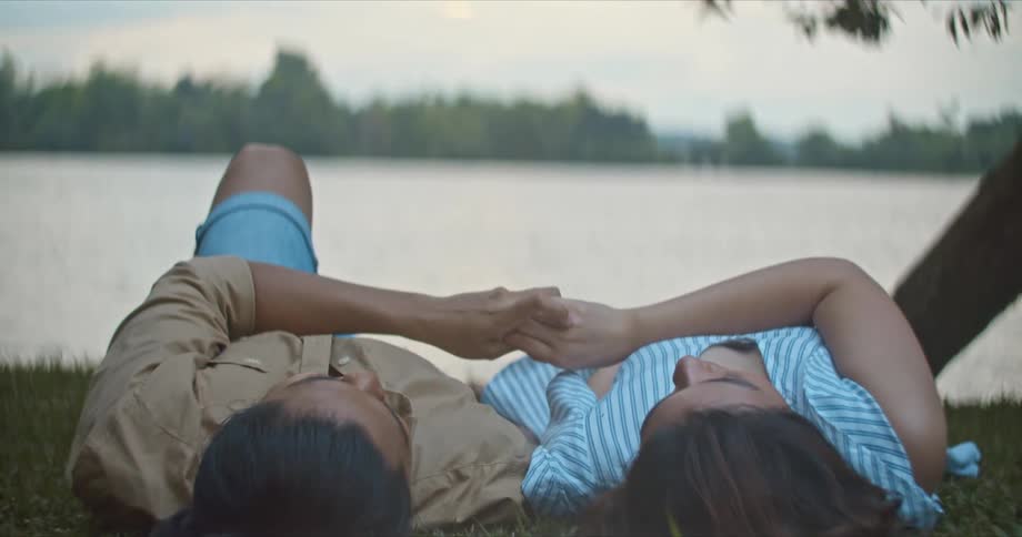 A couple is lying on the grass and holding hands