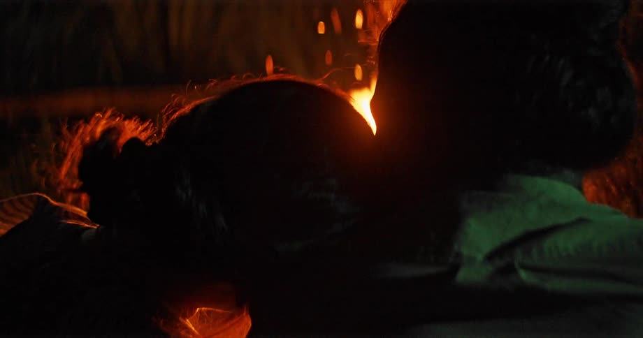 A man and woman sitting by a campfire with smoke and embers