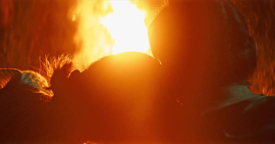 Man and woman sit side by side and watch campfire at night