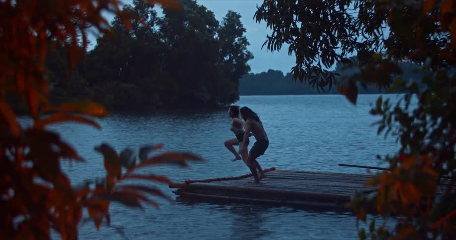 A man and woman hold hands as they jump off a dock in to the water