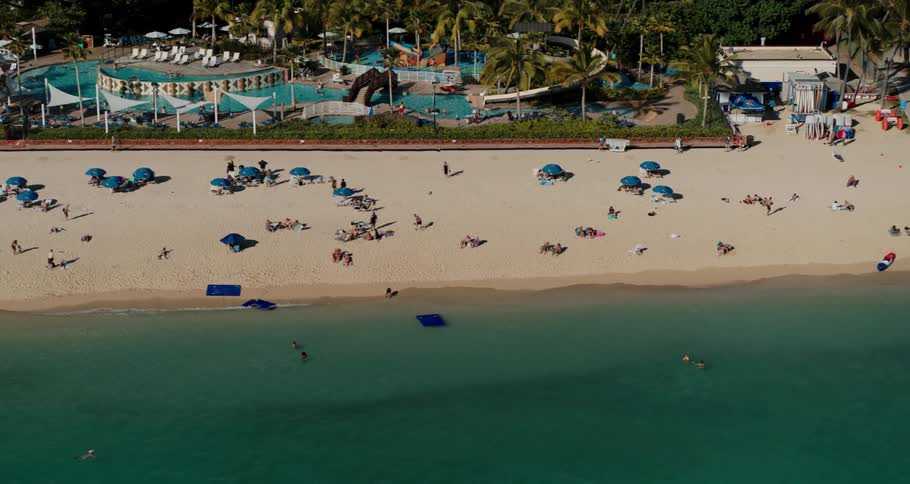 People occupy beach between blue green water and colorful park resort