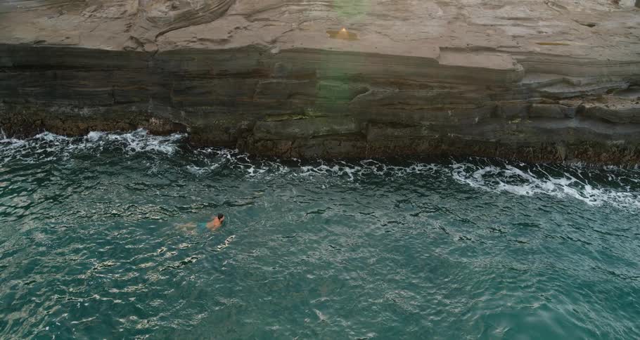 A person swims in water body near edge of a cliff