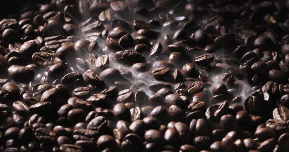 Vapor rises from brown coffee beans reflecting light