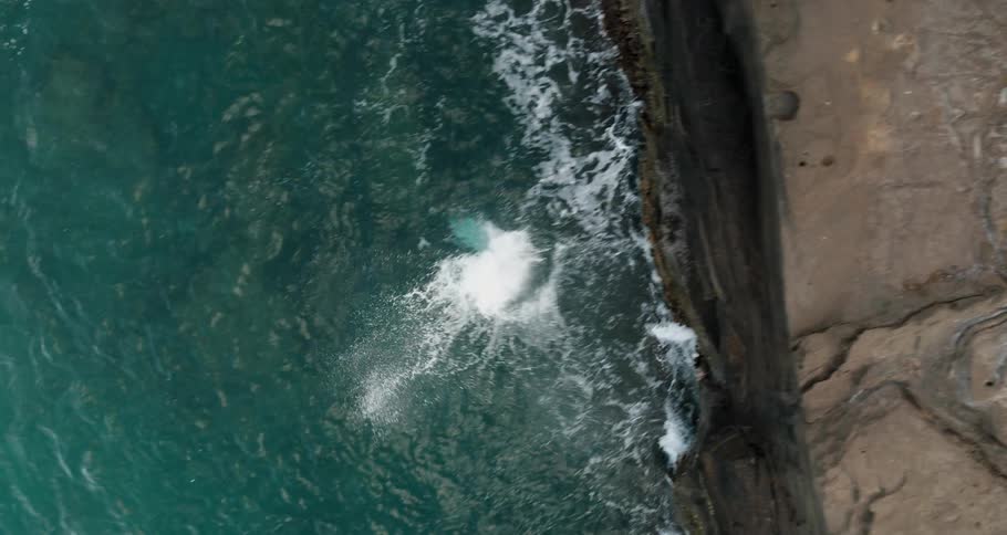 A man runs and dives off of a cliff tumbling and then splashing in the water