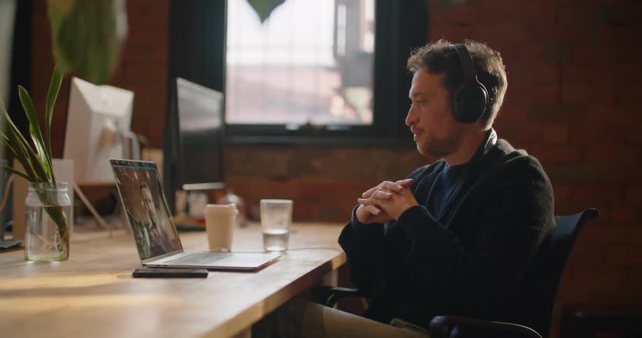 A man is talking on a video call on his laptop while sitting on a desk