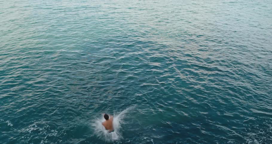 A man with shorts jumping off of a pier into water