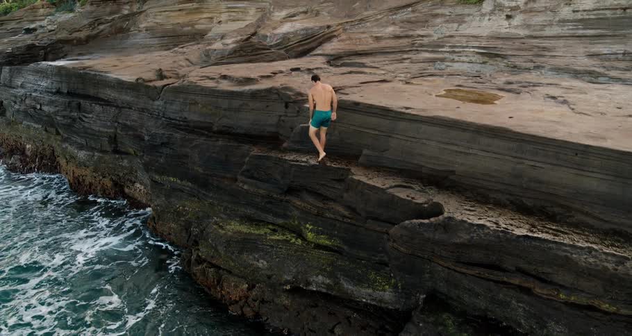 Man in green shorts climbs a cliff on the coast near the ocean