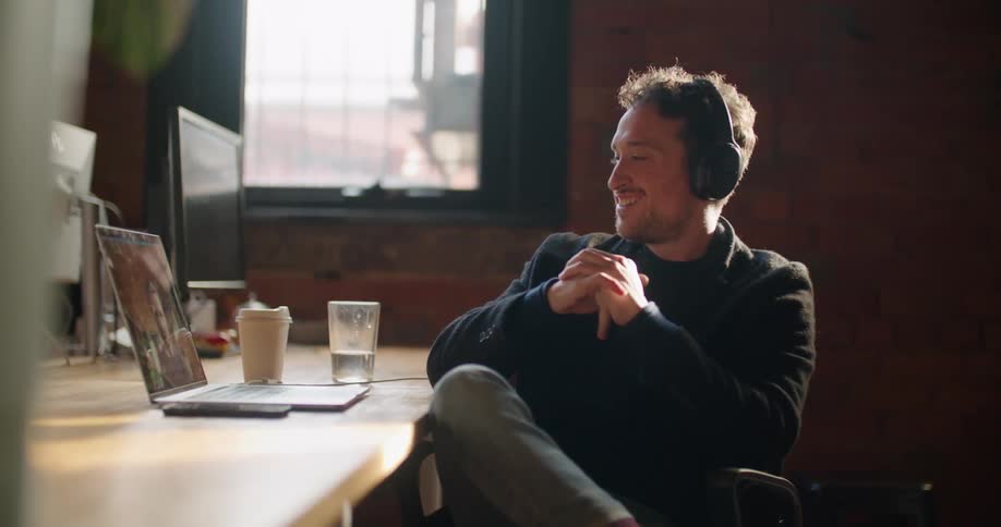 A man in an office talks with another man on a video call on his laptop